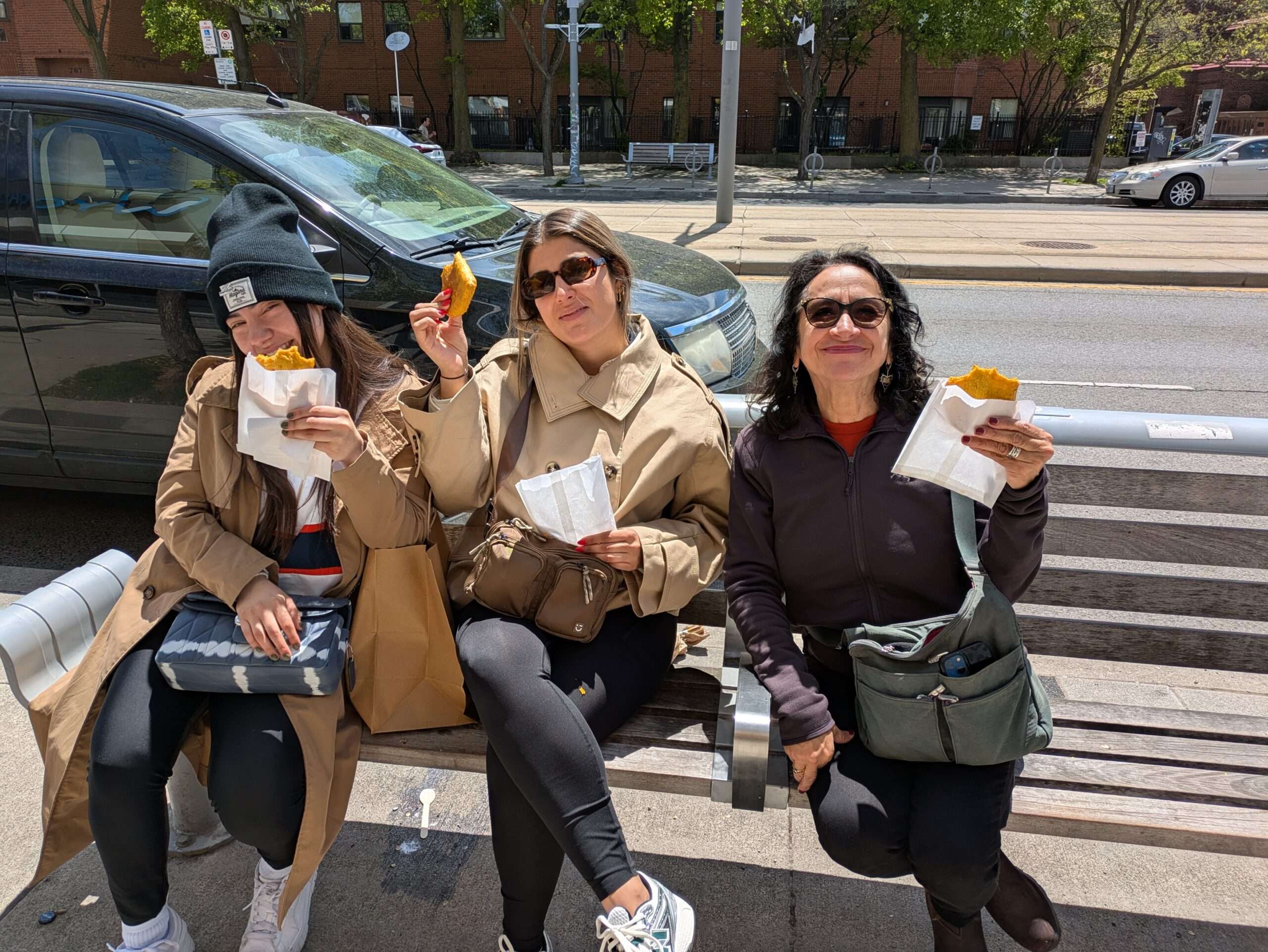 Friends on a food tour holding patties and sitting on a bench